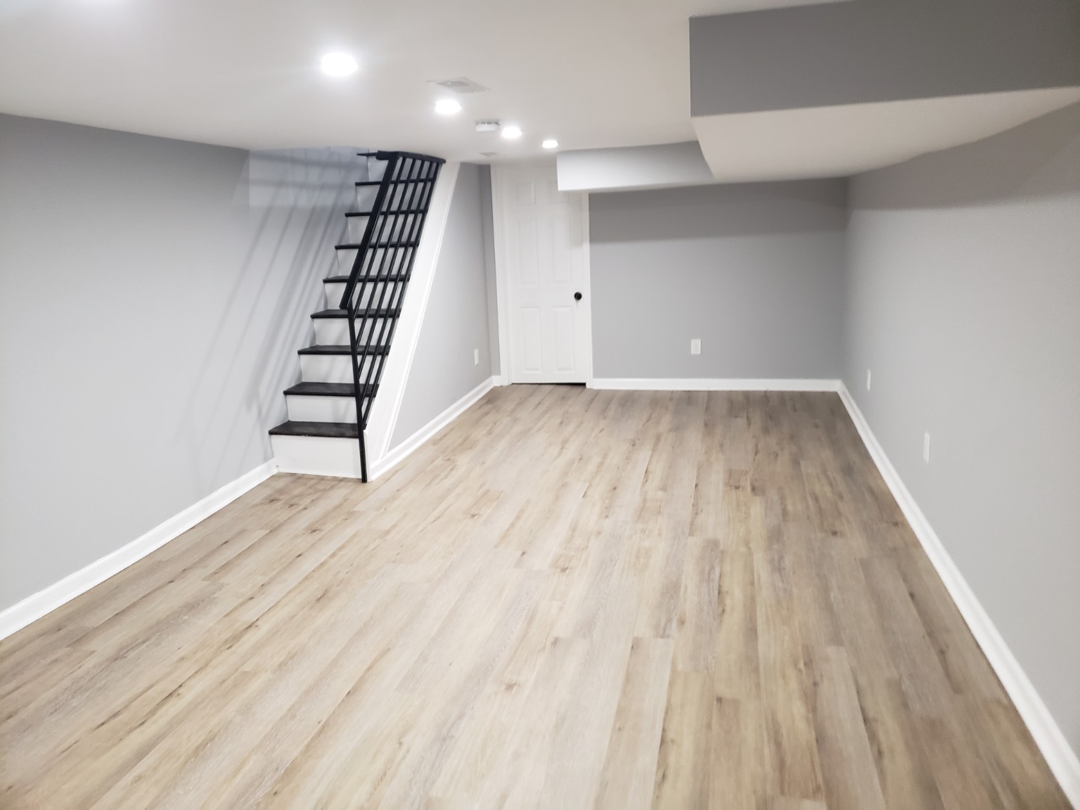 Finished basement with luxury vinyl plank flooring, gray walls, recessed lighting, and renovated stairs